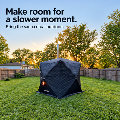 Black Willowybe sauna tent with a chimney and hanging lantern on a fenced backyard lawn at sunset