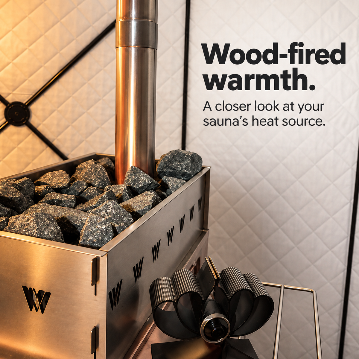 Close-up of rough sauna stones arranged around the chimney in a Willowybe wood-stove basket, with a fan shown beside the stove