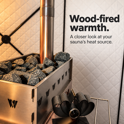 Close-up of rough sauna stones arranged around the chimney in a Willowybe wood-stove basket, with a fan shown beside the stove